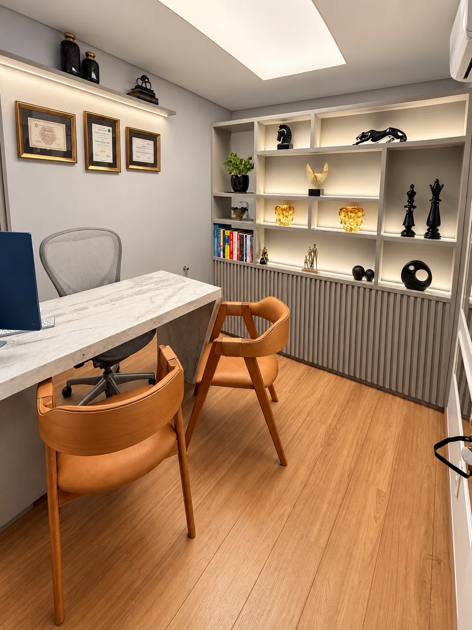 Consultório da Clínica Pelle com mesa de mármore claro, cadeiras caramelo e estante iluminada